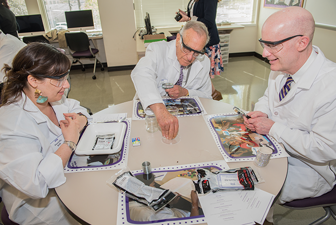 Chancellor Boschini, Paul Andrews, and a woman in lab coats utilizing math/science curriculum 