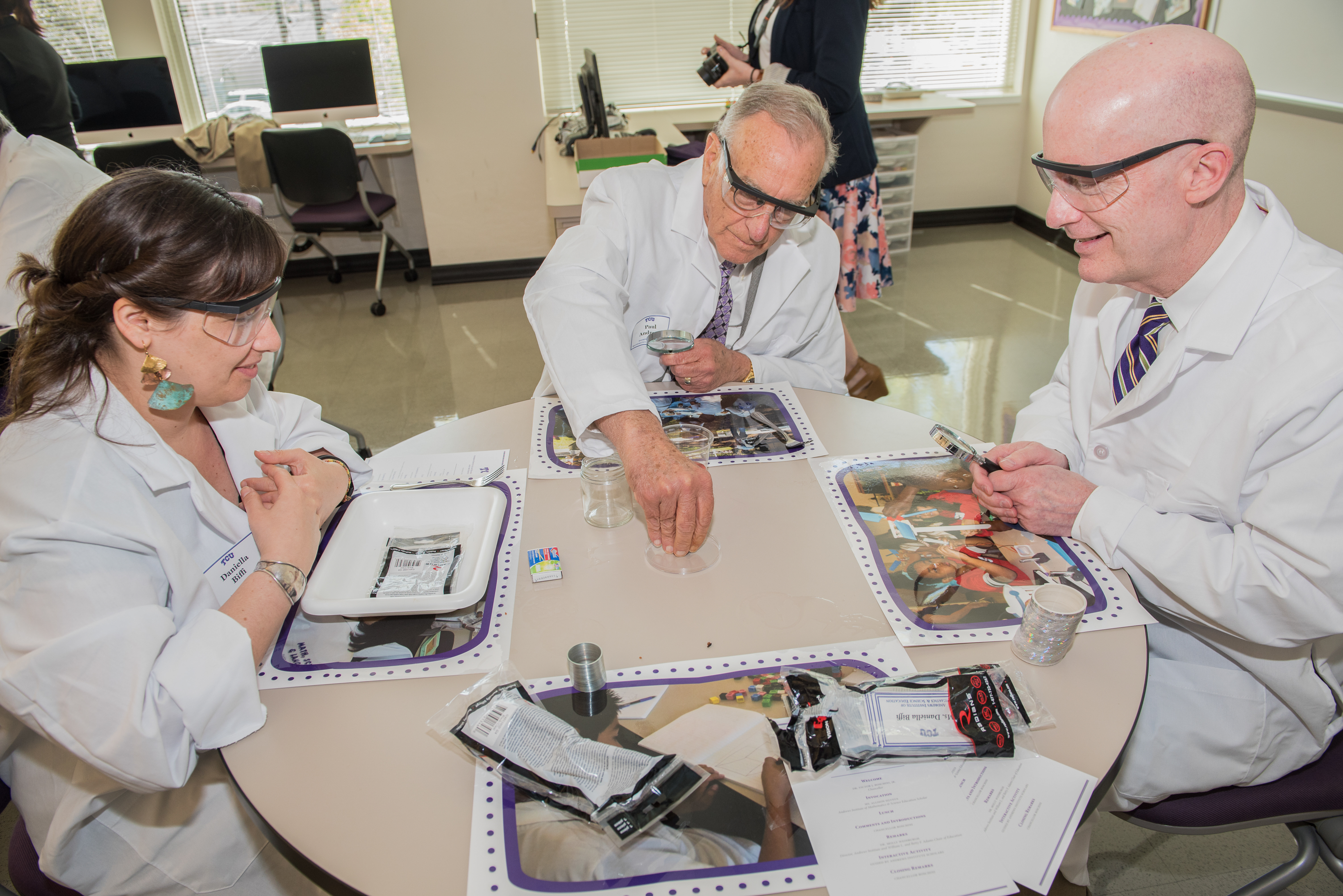 Chancellor Boschini, Paul Andrews, and a woman wearing white lab coats playing with math/science curriculum. 