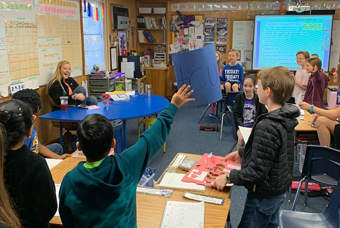 student teacher in classroom with students engaged and one raising hand