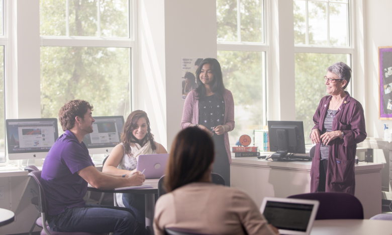 faculty looking at students in classroom while smiling