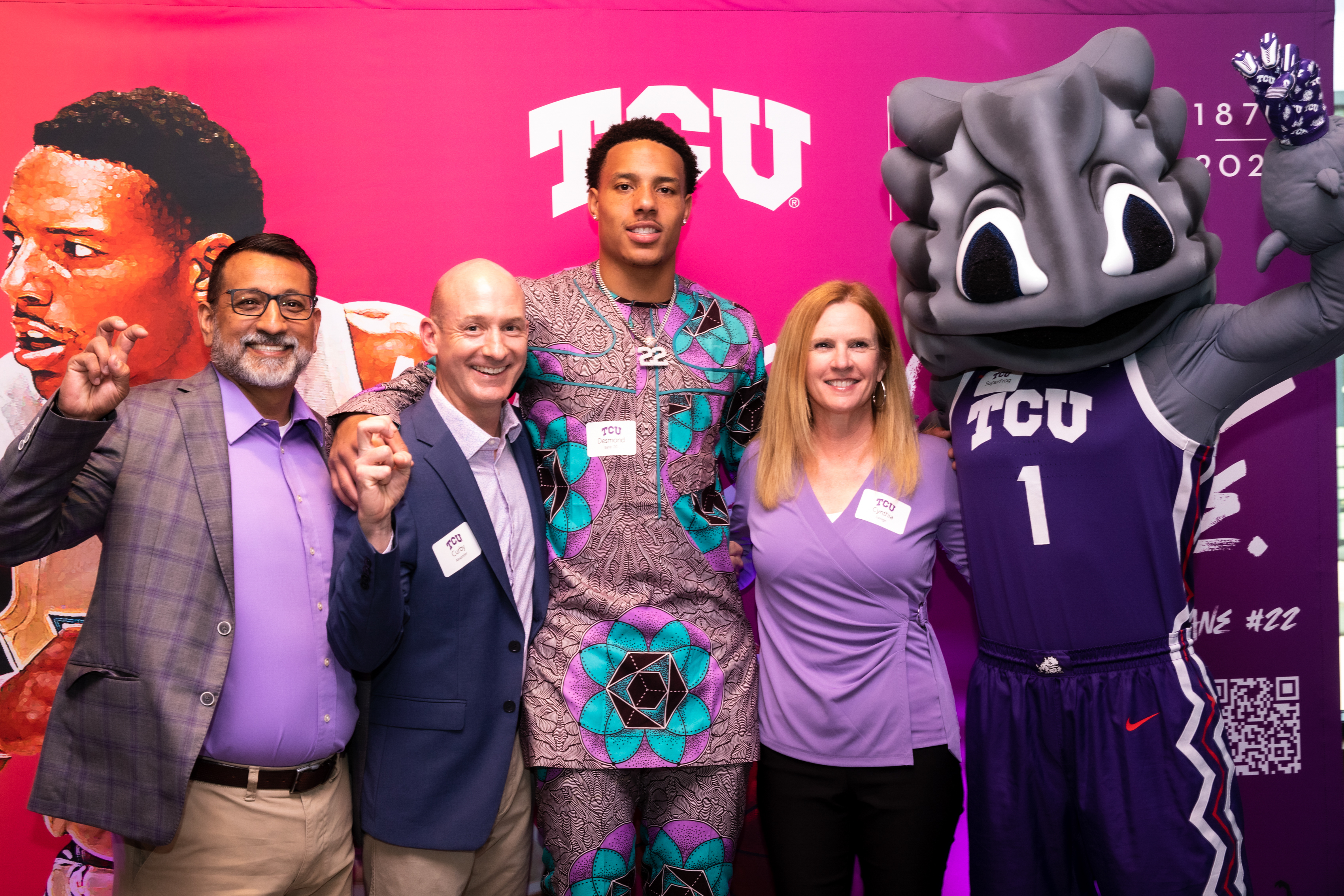 A group photo. From left to right: Dean Frank Hernandez, Professor Curby Alexander, Desmond Bane, Professor Cynthia Savage, and Super Frog. They stand in front of a pink and purple background with the TCU logo.
