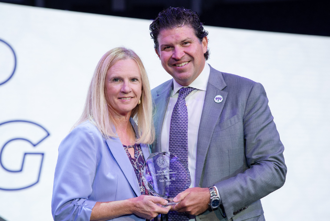 Cynthia Savage and Daniel Pullin. They hold a glass award and stand in front of a white background.