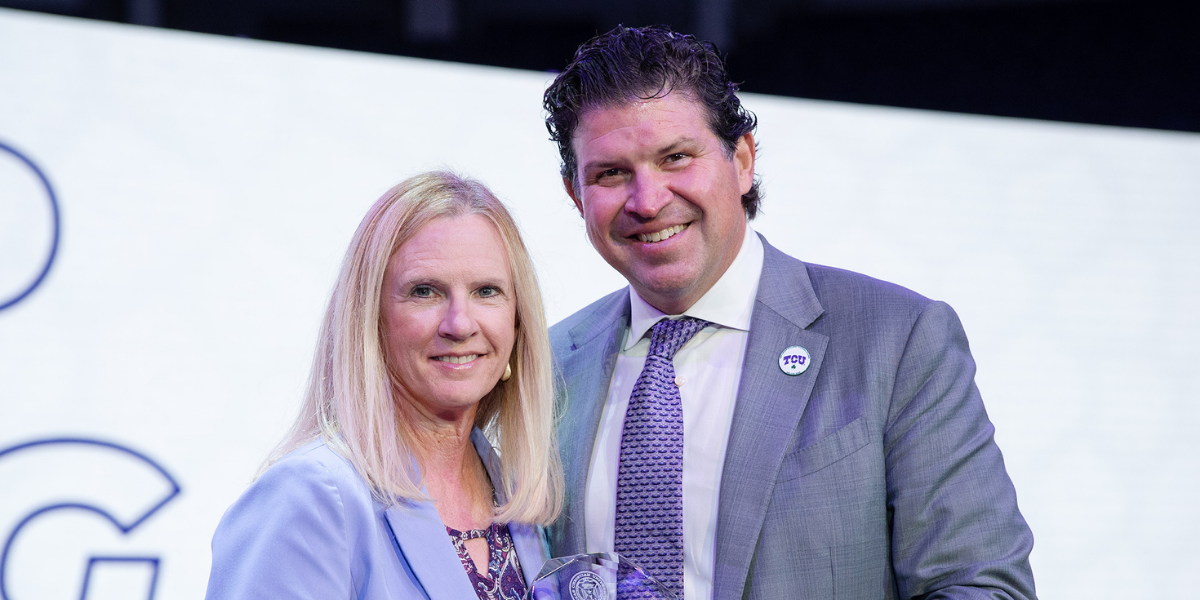 Cynthia Savage and Daniel Pullin. They hold a glass award and stand in front of a white background.