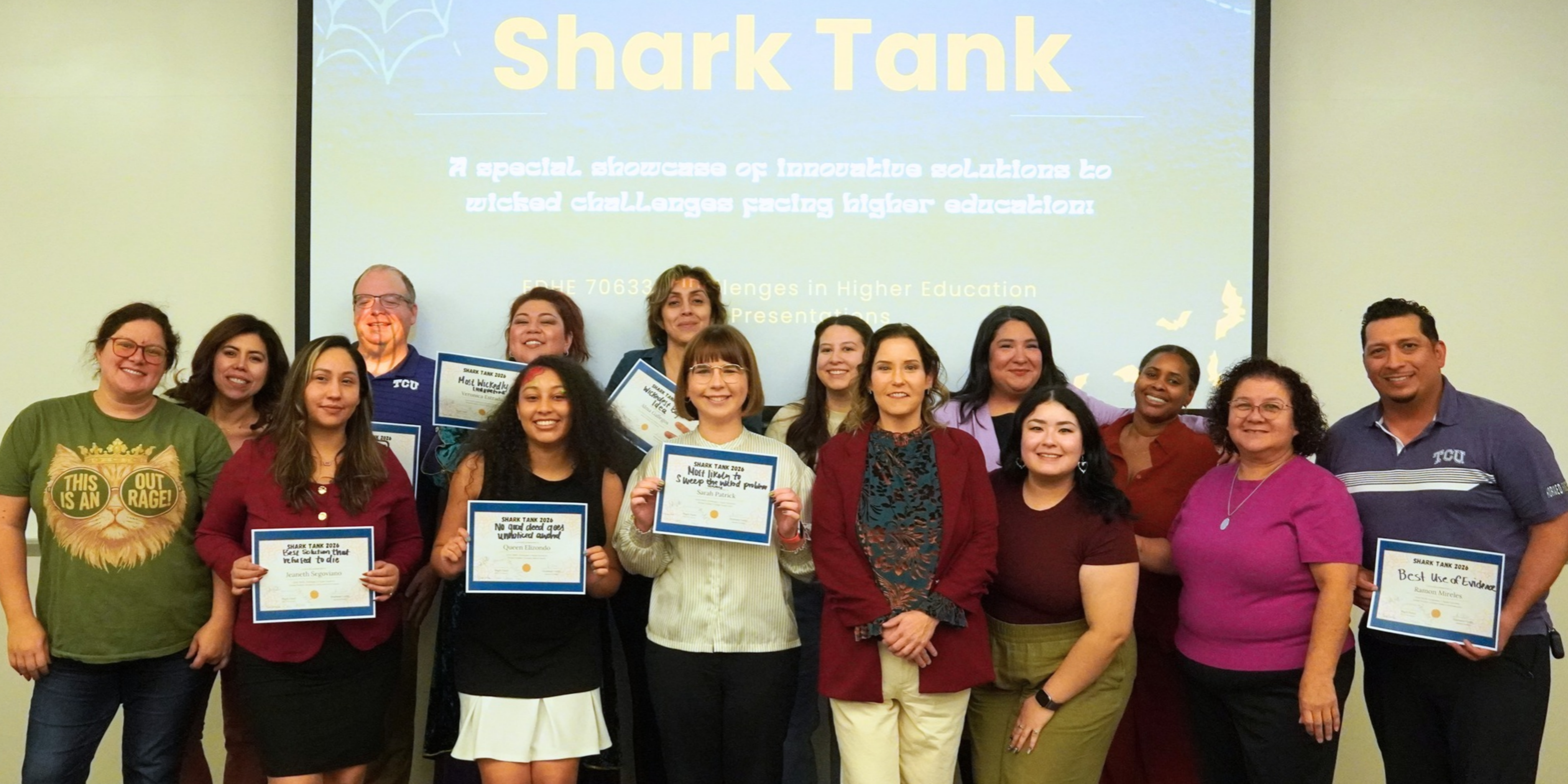 A group of individuals stand smiling in front of a "Shark Tank" presentation screen. Several are holding certificates. The background displays text related to higher education challenges.