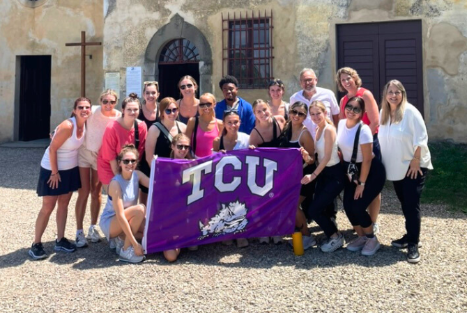 group photo of students and faculty smiling while holding TCU flag in Italy