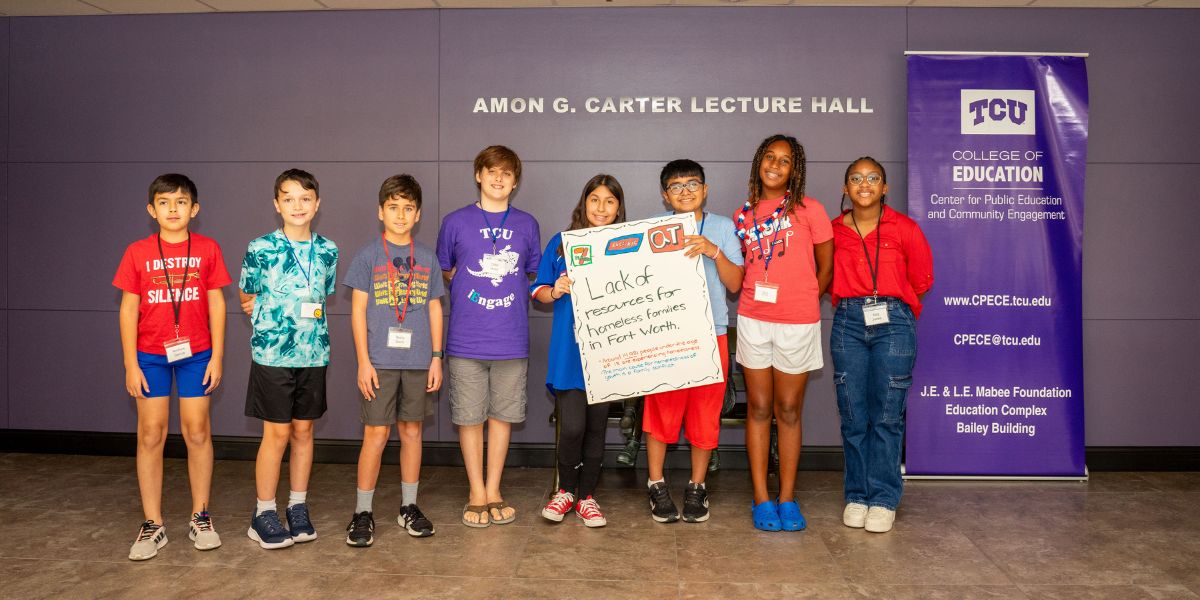 youth smiling at iengage camp holding sign "lack of resources for homeless families in Fort Worth"