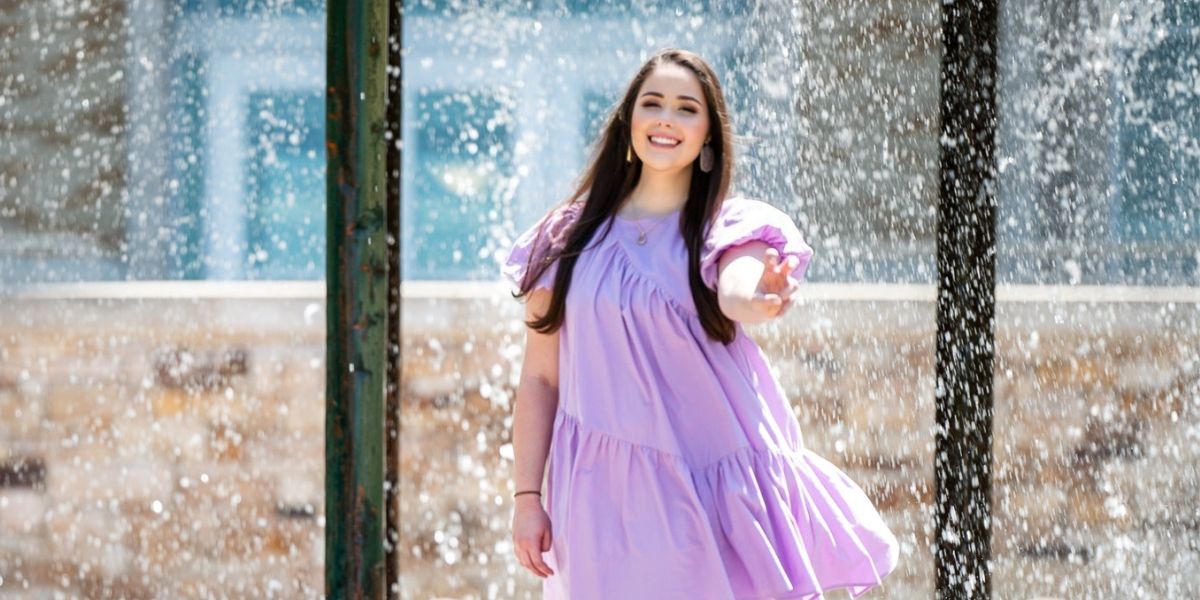 kaylee skinner smiling in purple dress with "horned frog" hand gesture in front of iconic TCU fountain